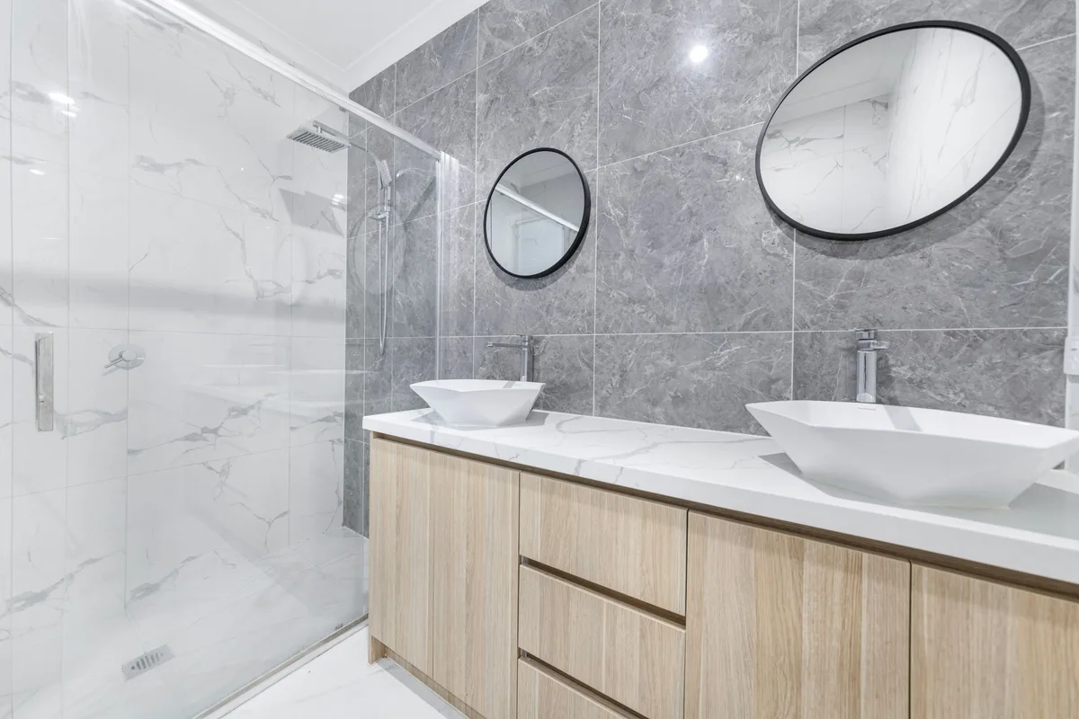 Modern bathroom with a wood vanity, two vessel sinks and marble-look wall tile