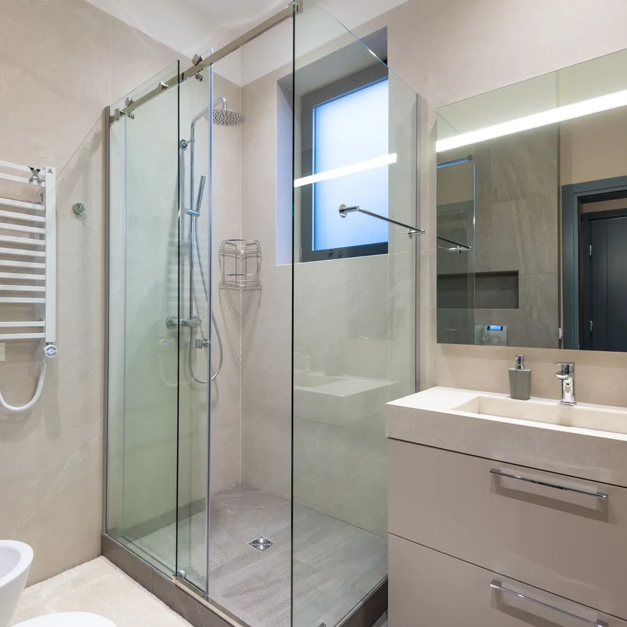Modern bathroom remodel with a glass shower enclosure, white vanity and beige wall tile