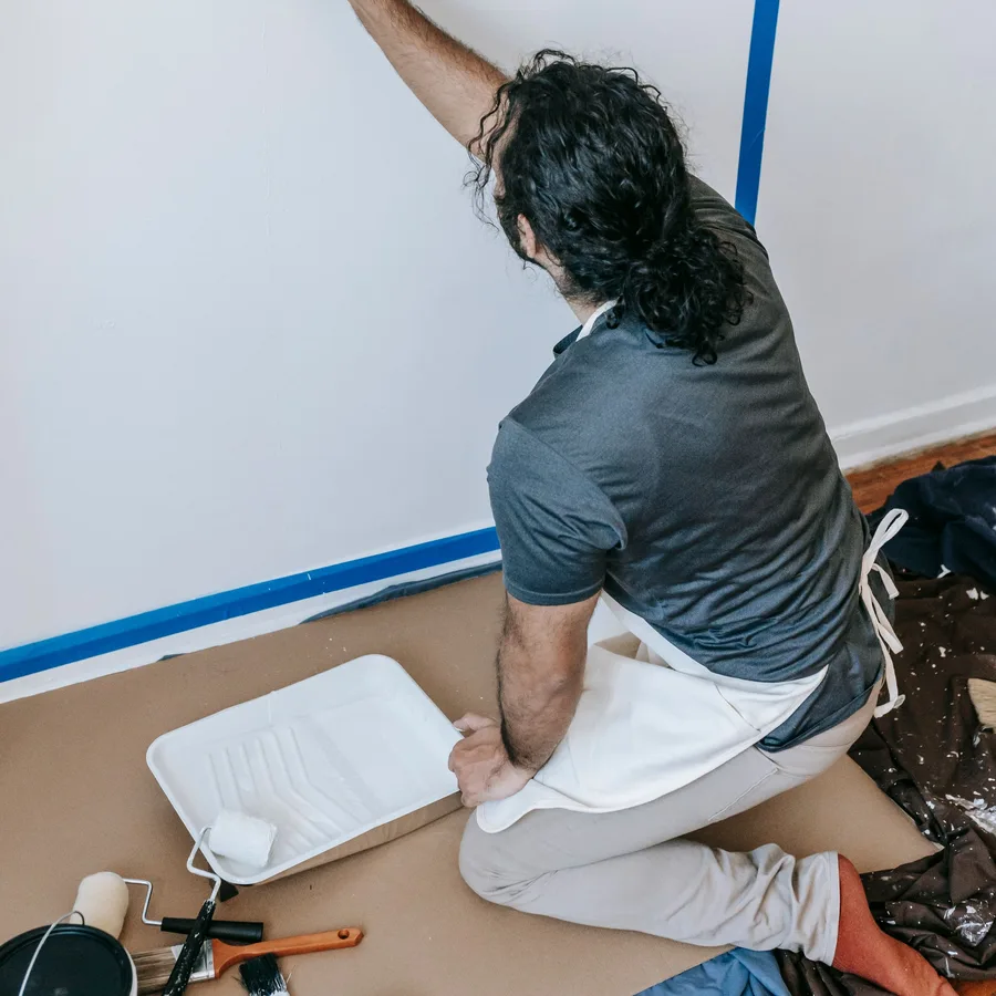 Painter cutting in a wall with a roller next to painter's tape and a drop cloth