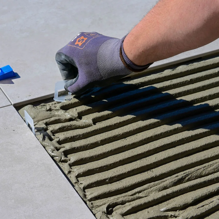 Installer setting a large porcelain floor tile with leveling clips over thinset