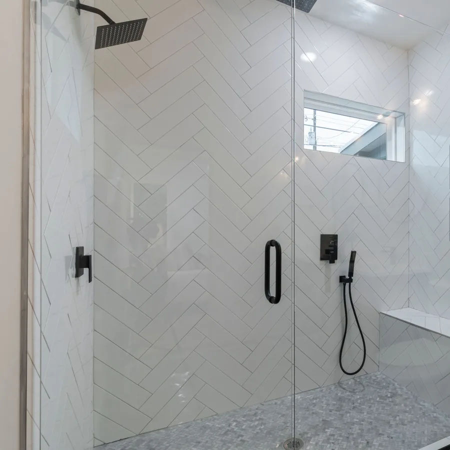 Large walk-in shower with white herringbone tile, a built-in niche and black fixtures